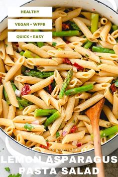 a pan filled with pasta and asparagus next to a wooden spoon