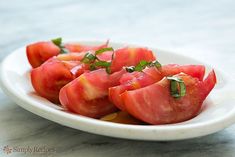 a white plate topped with sliced tomatoes on top of a marble countertop and garnished with green leaves