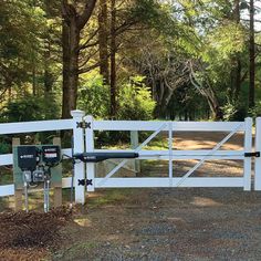 a white gated driveway leading to a wooded area with trees in the back ground