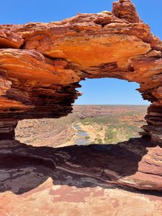 an arch shaped rock formation on the edge of a cliff with a river in the distance