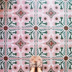 a person standing in front of a pink and green tile wall with flowers on it