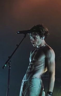 a man with no shirt on standing in front of a microphone and holding a mic