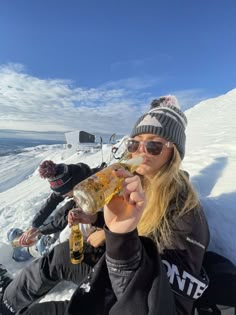 two people sitting in the snow and one is holding up a beer bottle to her mouth