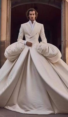 a man in a white suit and tie is standing on a giant dress made out of cloths