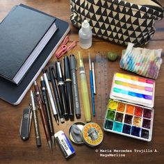 the contents of a travel bag laid out on top of a wooden table, including pens, markers and pencils