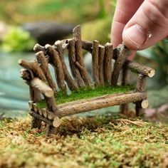 a miniature bench made out of wood and moss is being held by someone's hand