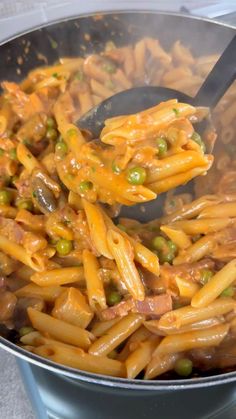 a pot filled with pasta and peas being stirred by a ladle