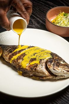 a person pouring sauce onto a fish on a plate