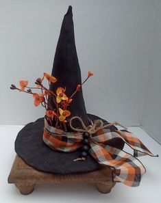 a black hat with orange flowers and ribbon tied around it on top of a wooden stand