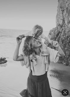 a woman holding a child on her shoulders near the ocean