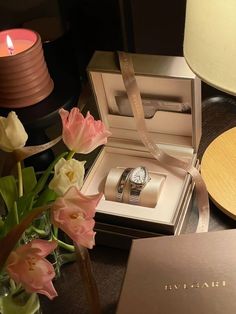 a watch and flowers on a table next to a lamp with a candle in it