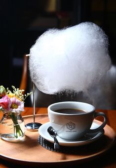 a cup of coffee on a saucer with cotton floss in the air above it