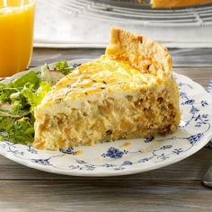 a piece of quiche on a blue and white plate next to a glass of orange juice