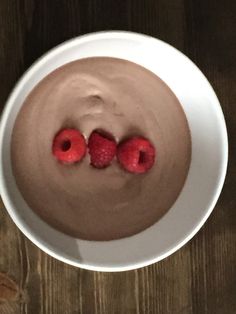 two raspberries on top of a chocolate dessert in a white bowl with dark wood background