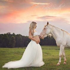 a woman in a wedding dress standing next to a white horse on a lush green field