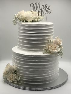 a wedding cake with white flowers and mr and mrs topper on the bottom tier