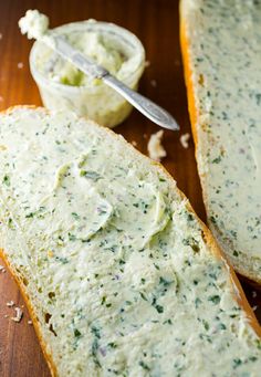 two pieces of bread with cheese spread on them and a spoon next to it, sitting on a wooden surface