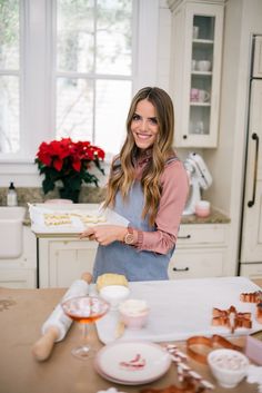 a woman is standing in the kitchen holding a tray with food on it and smiling at the camera