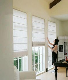 a woman standing next to a window in a living room with white furniture and windows