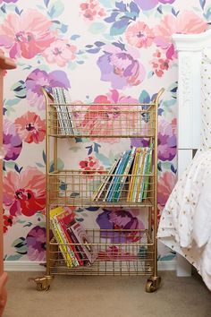 a gold metal book rack with books on it in front of a floral wallpaper