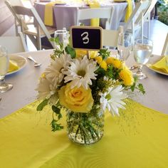 a vase filled with yellow and white flowers on top of a table covered in tables cloths