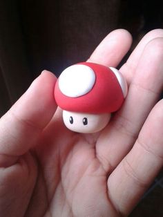 a hand holding a red and white mushroom toy in it's left palm area