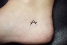 a small tattoo on the foot of a person with a triangle and an arrow in it