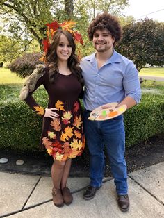 a man standing next to a woman in a dress holding a plate with leaves on it