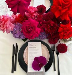 the table is set with black and white plates, silverware, and red flowers