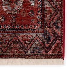 a red rug with an intricate design on the bottom and fringes around the edges