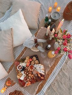 a table topped with food and candles on top of a beach covered in sand next to water