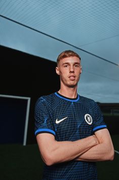 a young man standing in front of a soccer ball wearing a blue shirt and holding his arms crossed