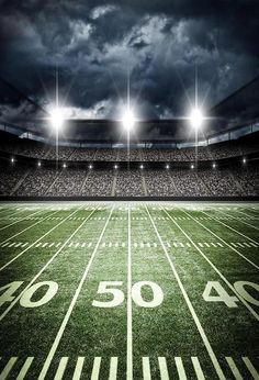 an empty football field at night with the lights on and dark clouds in the sky