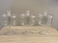 three clear glass containers with lids on top of a wooden table next to a wall