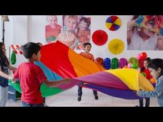 two children are playing with a rainbow colored kite in a room full of other kids