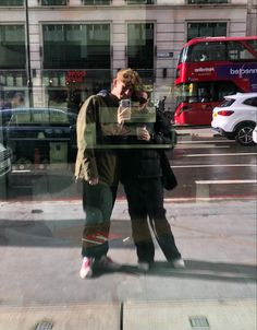 two people standing in front of a window on a city street with cars behind them