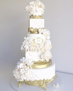 a three tiered white and gold wedding cake with flowers on the top, sitting on a table