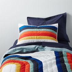 a bed with blue, orange, yellow and white comforter on top of it