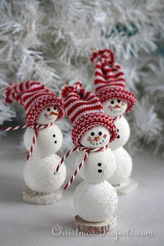 three snowmen with hats and candy canes in front of a white christmas tree