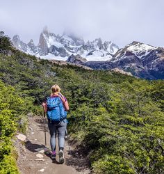 a woman hiking up a trail with mountains in the backgrouds behind her