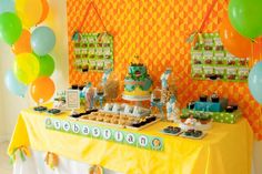 a table topped with lots of desserts and balloons next to a wall covered in orange and green