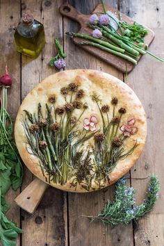 a pizza with herbs on it sitting on top of a wooden table next to other vegetables