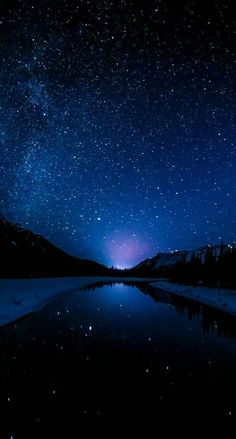 the night sky with stars above a lake and mountain range in the foreground is reflected in water