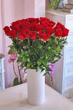 a white vase filled with red roses on top of a table