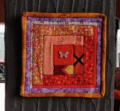 an orange and purple quilt hanging on the side of a tree