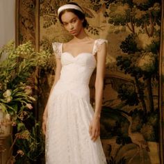 a woman standing in front of a painting wearing a white dress and headband with flowers on it