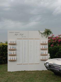 a white car parked next to a wall with shelves on it's sides and flowers in the background