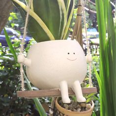 a white plastic toy sitting on top of a potted plant in a hanging basket