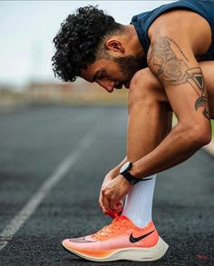 a man tying his shoelaces on the side of an empty parking lot while wearing nike running shoes