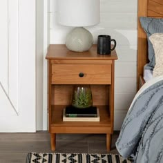 a nightstand with a lamp on top of it next to a bed